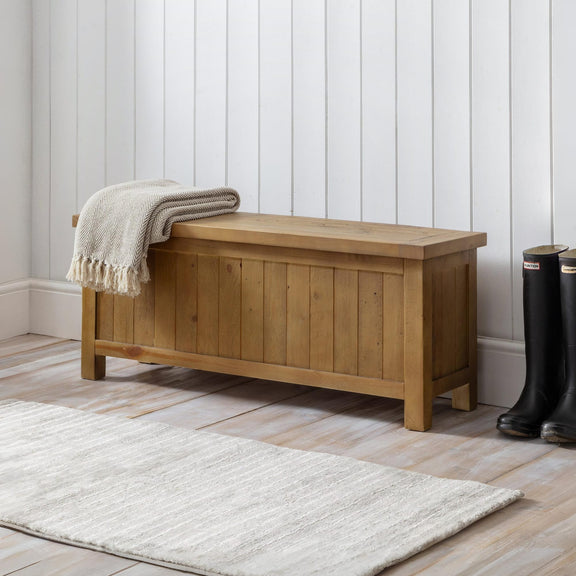 Wooden storage bench with a blanket and boots in a room with white paneled walls and a wooden floor.