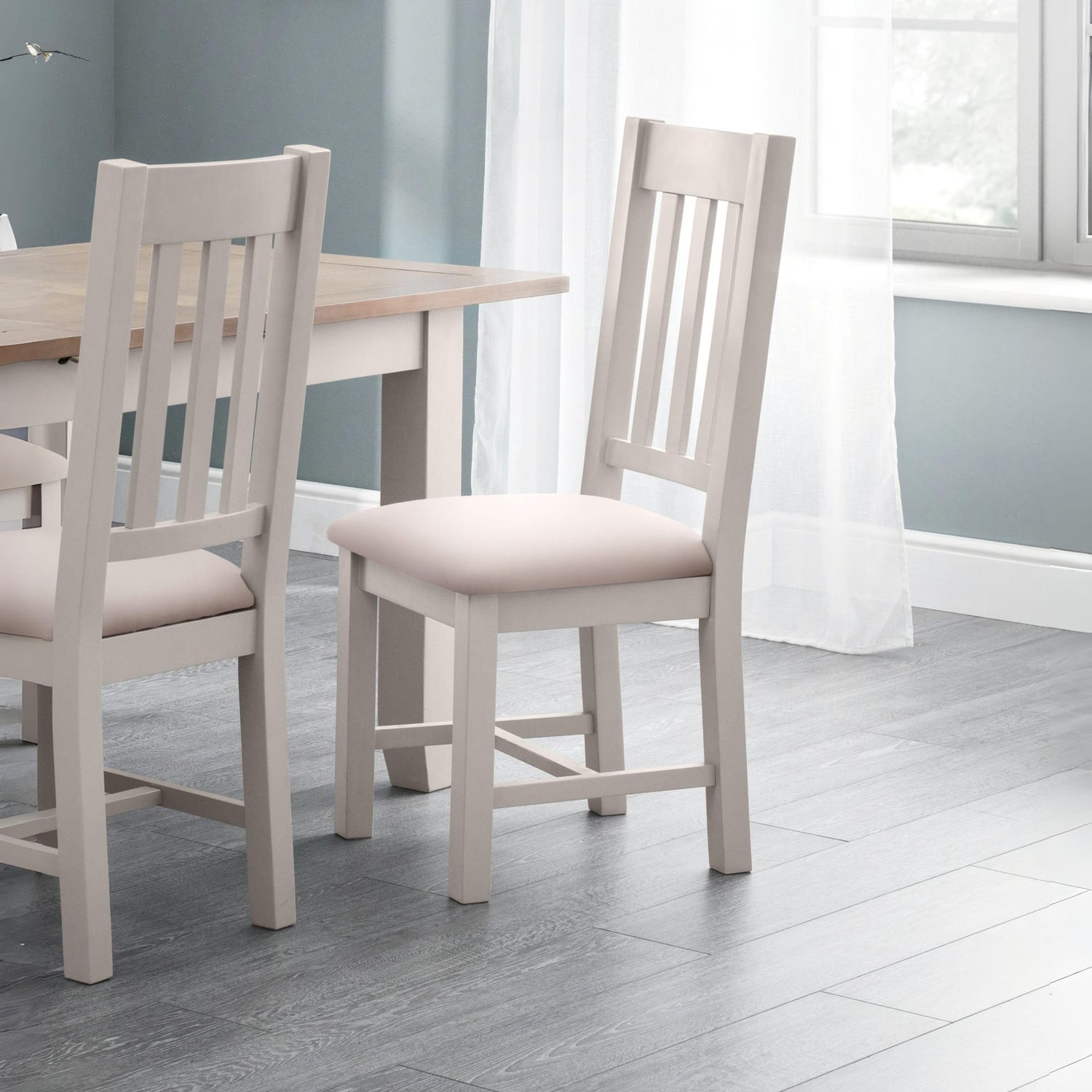 Dining table with two chairs in a room with light gray walls and wooden flooring.