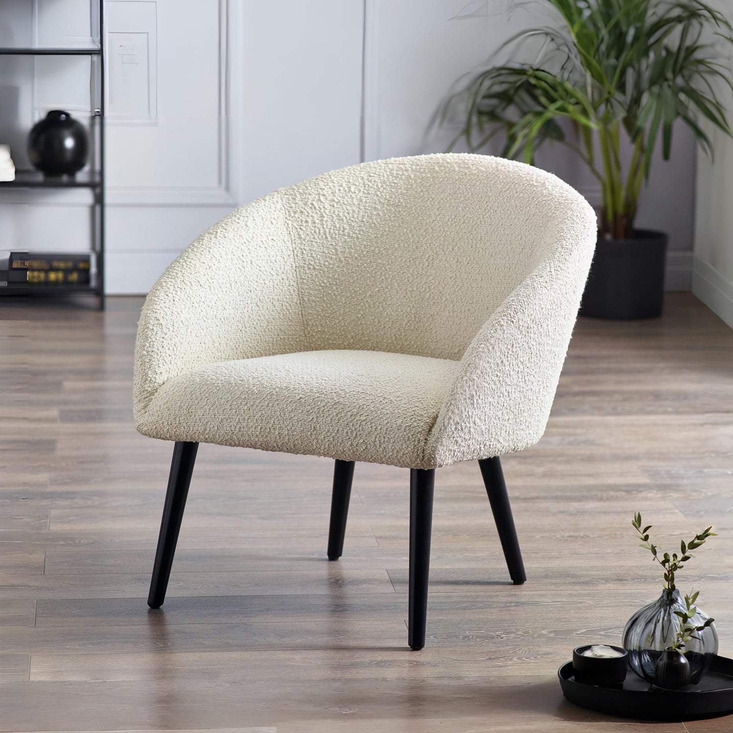 Cream-colored armchair with black legs in a room with a plant and decorative items.
