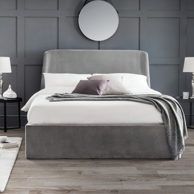 Gray upholstered bed with white bedding in a room with gray walls and wooden flooring.