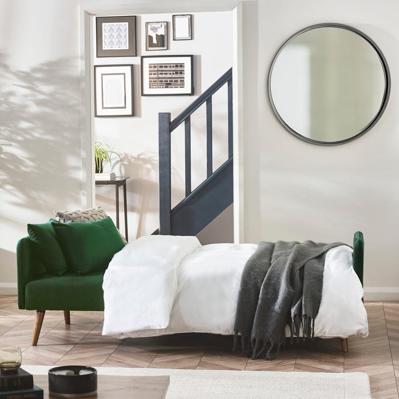 Modern bedroom with green armchair, bed, and round mirror.