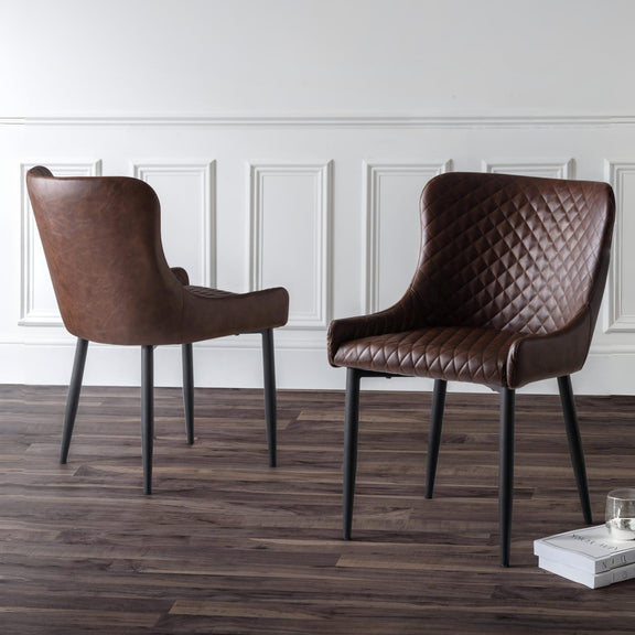 Two brown leather chairs on a wooden floor with a white paneled wall in the background.