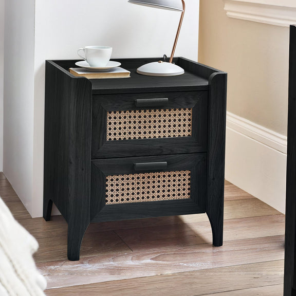 Black wooden bedside table with rattan drawer fronts beside bed