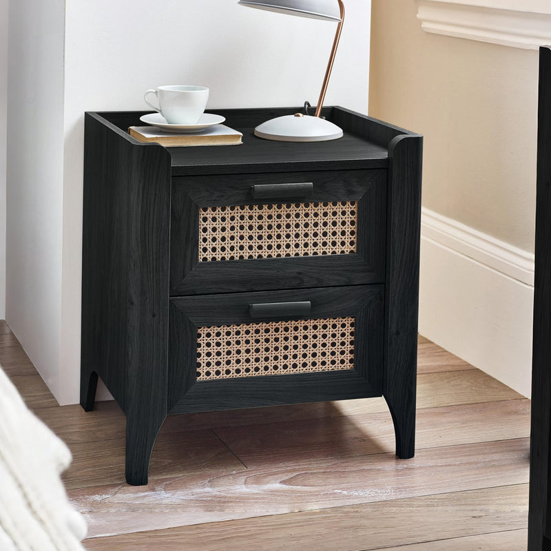 Black wooden bedside table with rattan drawer fronts beside bed