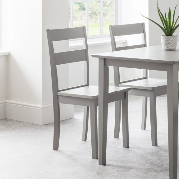 Gray dining table with two matching chairs in a bright room.