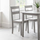 Gray dining table with two matching chairs in a bright room.