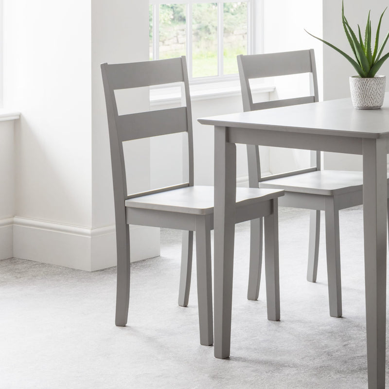 Gray dining table with two matching chairs in a bright room.