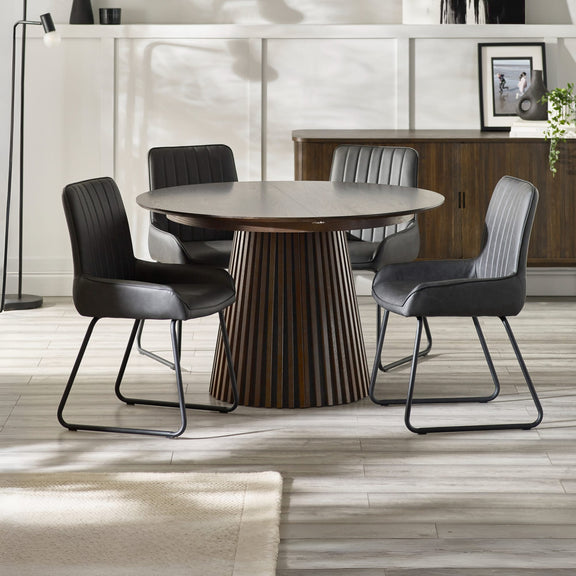 Round wooden dining table with four black chairs in a modern room.