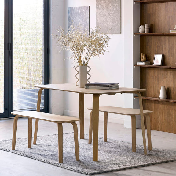 Dining area with a light wood table and benches in a modern room.