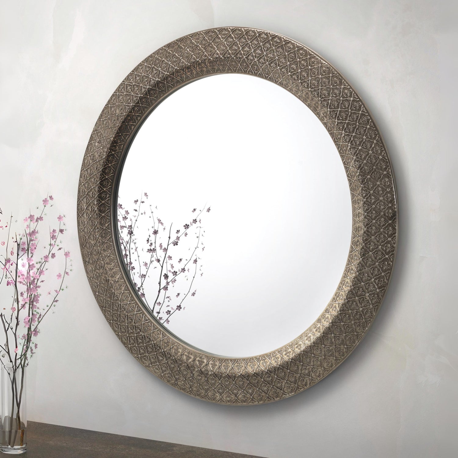 Decorative round mirror with intricate design on a plain wall.