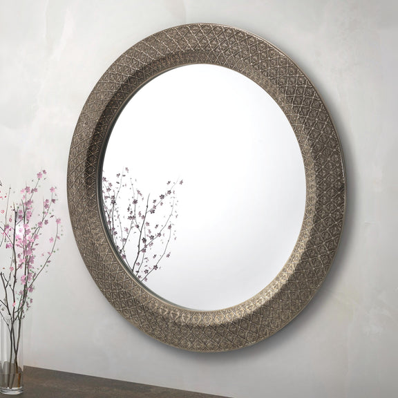Decorative round mirror with intricate design on a plain wall.