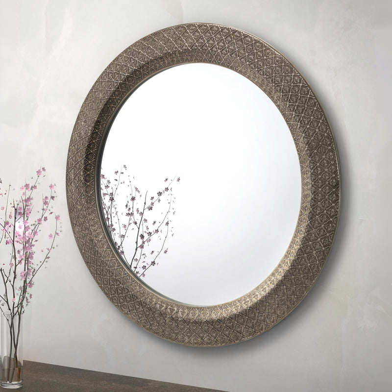 Decorative round mirror with intricate design on a plain wall.