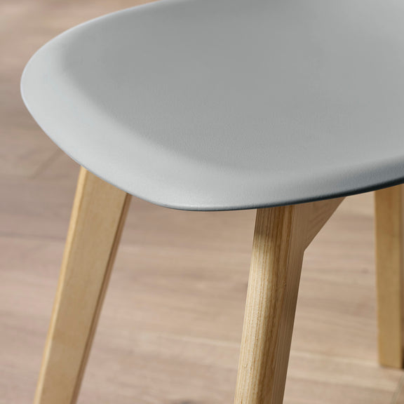 Close-up of a chair with a light gray seat and wooden legs on a wooden floor.