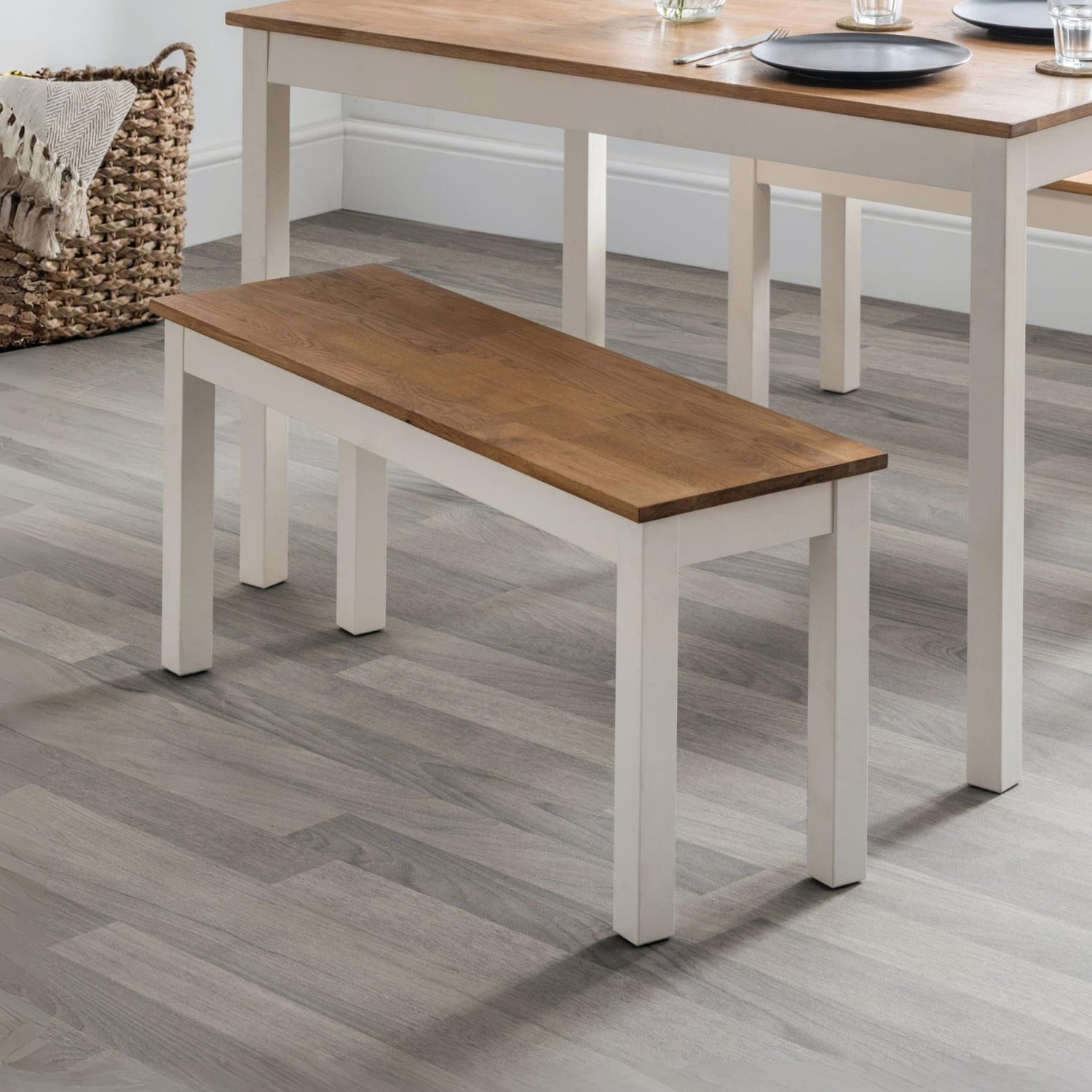 Wooden bench with white base in front of a wooden table on a gray floor.