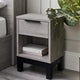 Wooden nightstand with a drawer and shelf, books, and a plant in a bedroom setting.