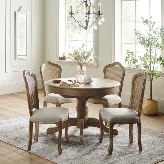 Round wooden dining table with four chairs in a well-lit room with large windows.