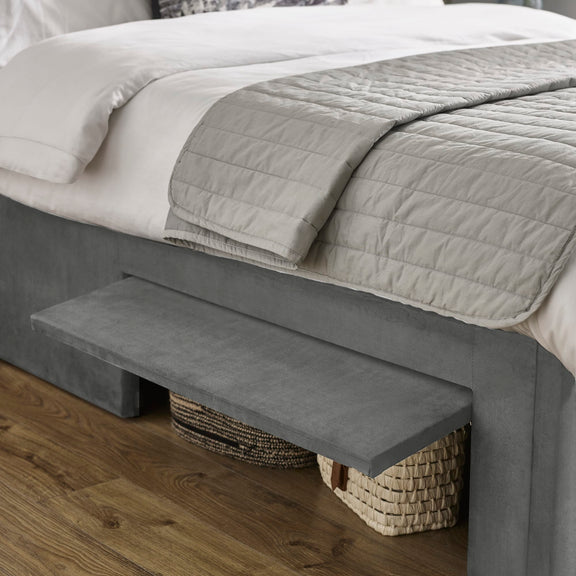 Gray upholstered bench at the foot of a bed with a textured blanket