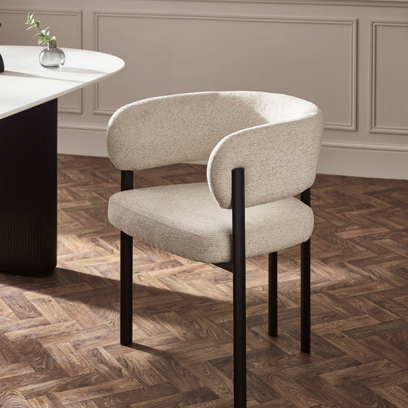 Beige chair with black legs on a wooden floor in a room with a neutral color scheme.