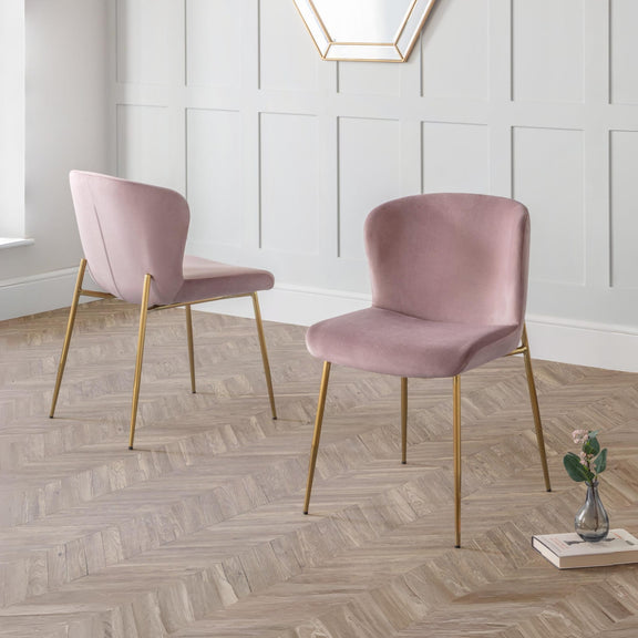 Two pink velvet chairs with gold legs on a wooden floor.