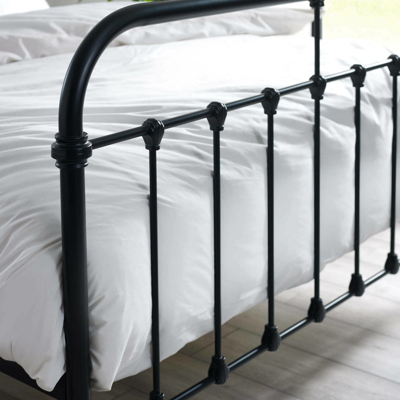 Black metal bed frame with white bedding on a wooden floor.