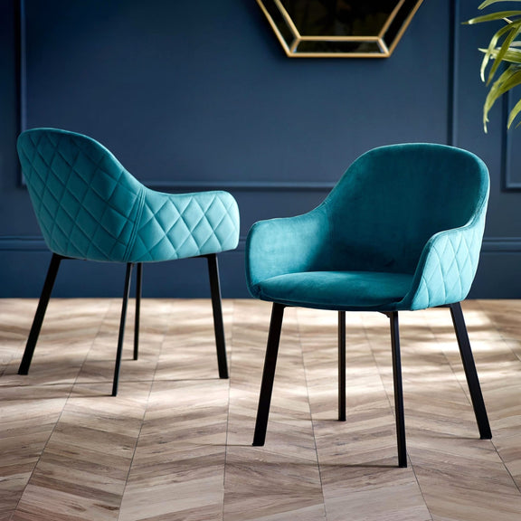 Two teal chairs with black legs on a wooden floor against a blue wall.