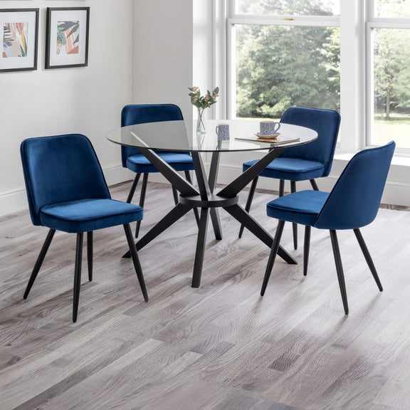 Dining room with a round glass table and four blue chairs on a wooden floor.