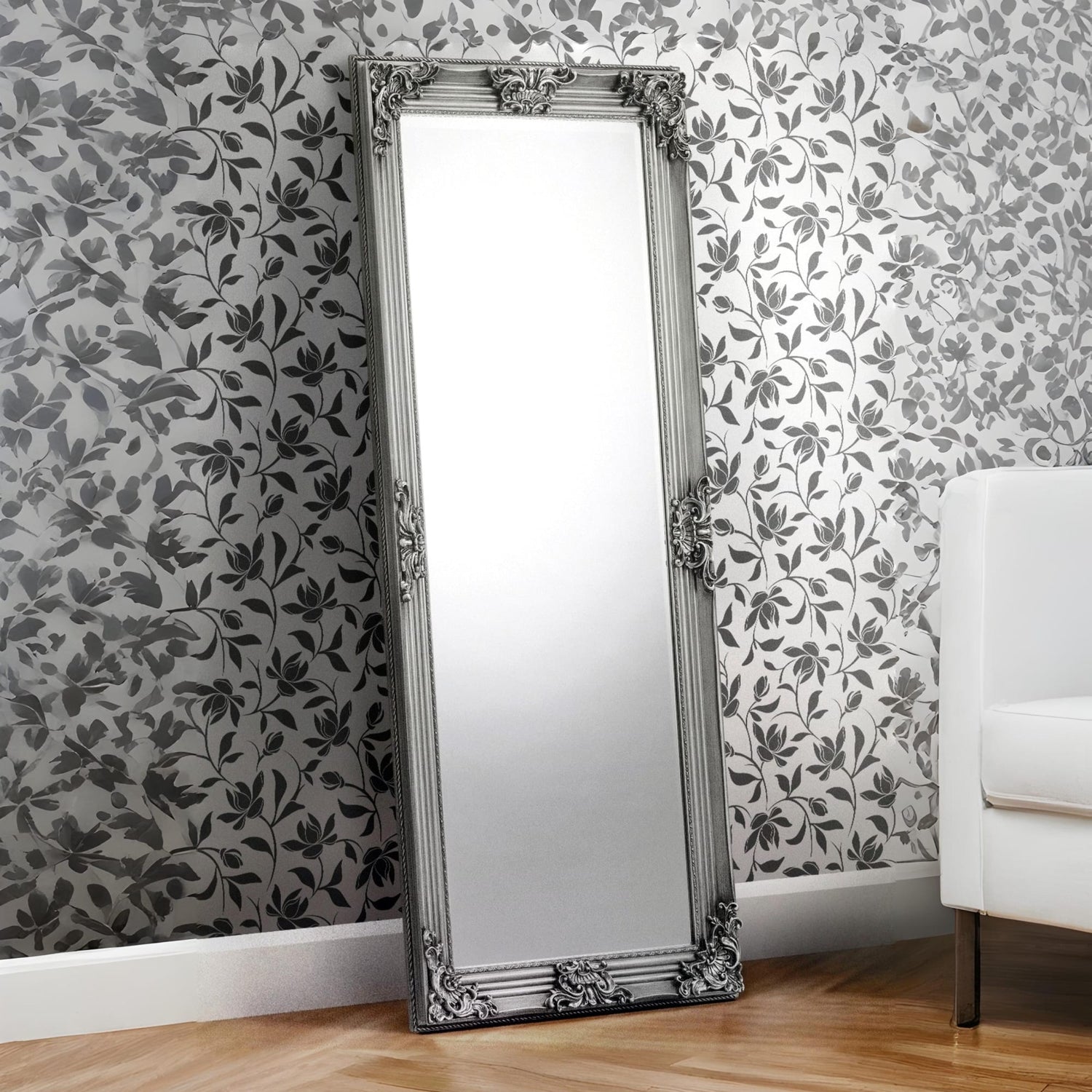 Decorative floor mirror with ornate frame against a floral wallpapered wall.