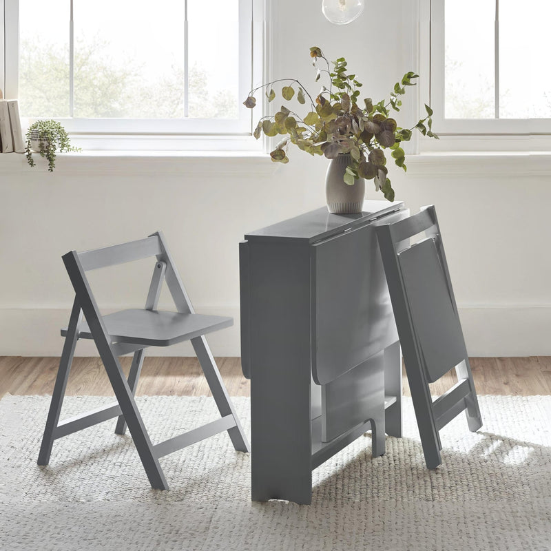 Gray dining table with two matching chairs in a bright room with large windows.