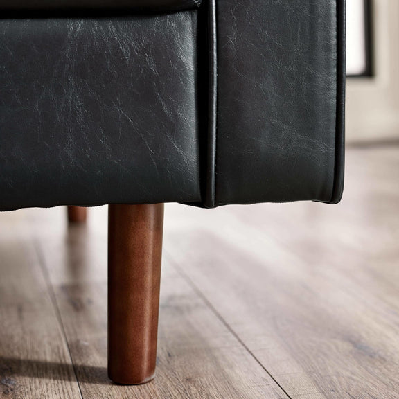 Close-up of a black leather armchair with wooden legs on a wooden floor.