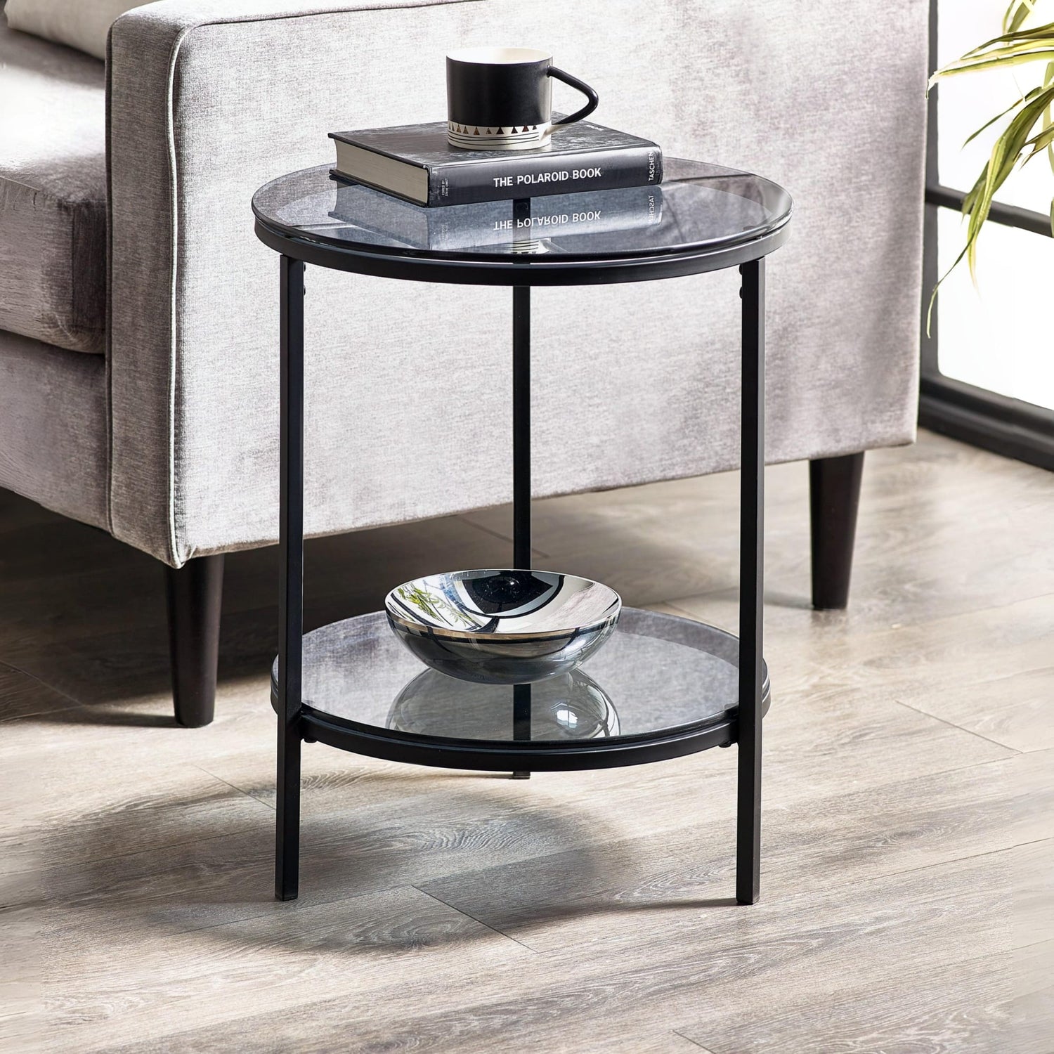 Round glass side table with black metal frame in a living room setting.