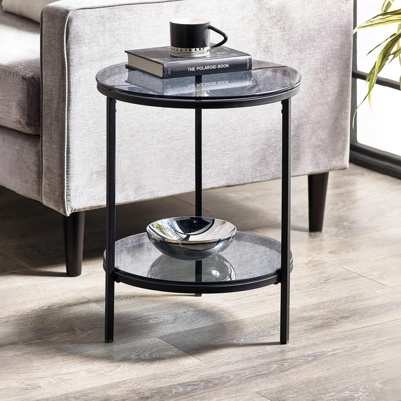 Round glass side table with black metal frame in a living room setting.