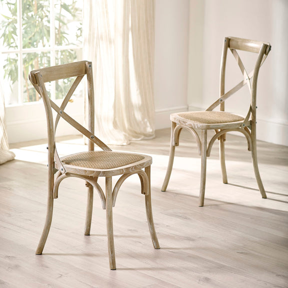 Two wooden chairs with woven seats in a bright room with white curtains.