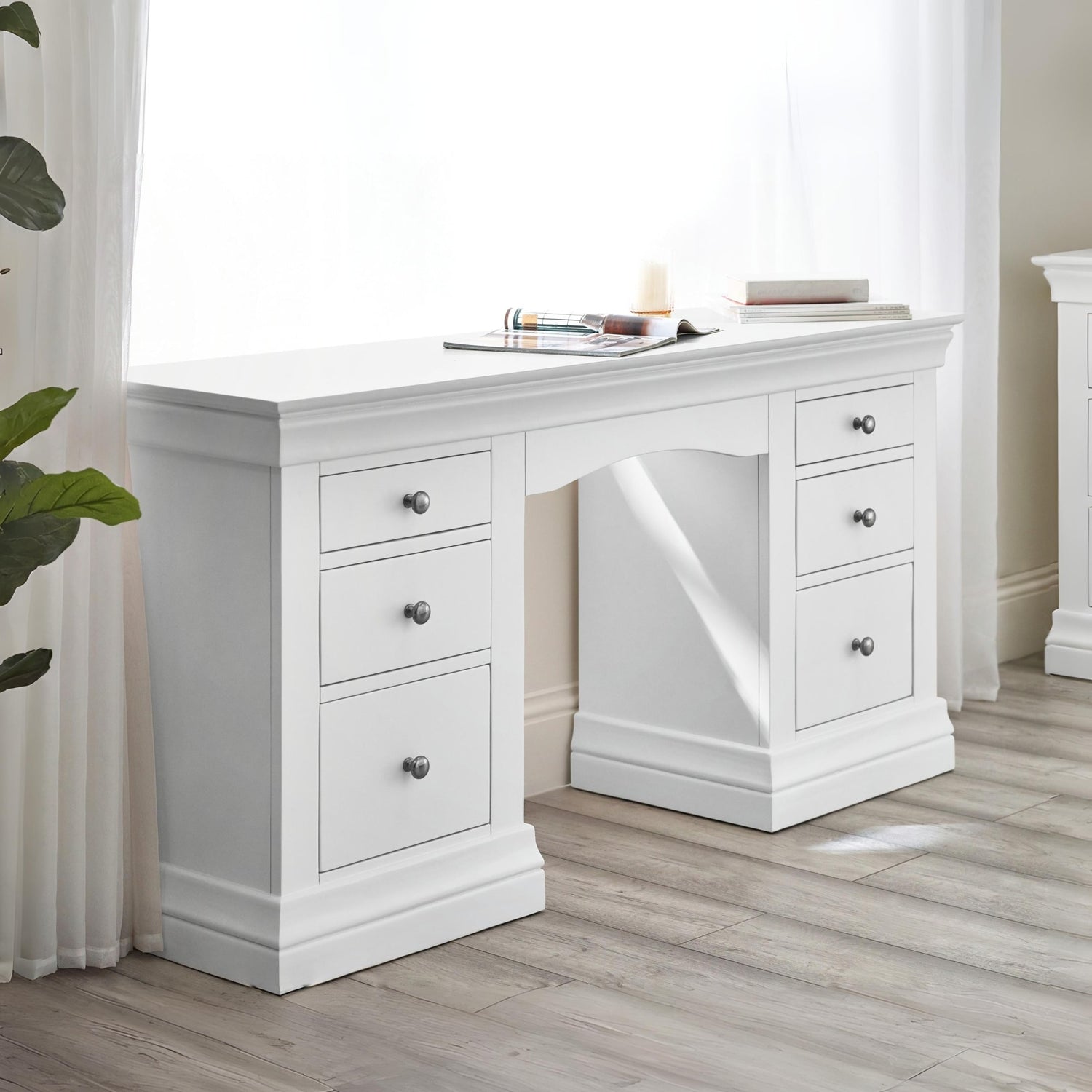 White desk with multiple drawers in a room with light wood flooring and white walls.