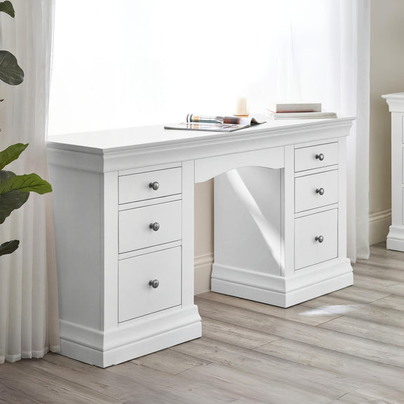 White desk with multiple drawers in a room with light wood flooring and white walls.