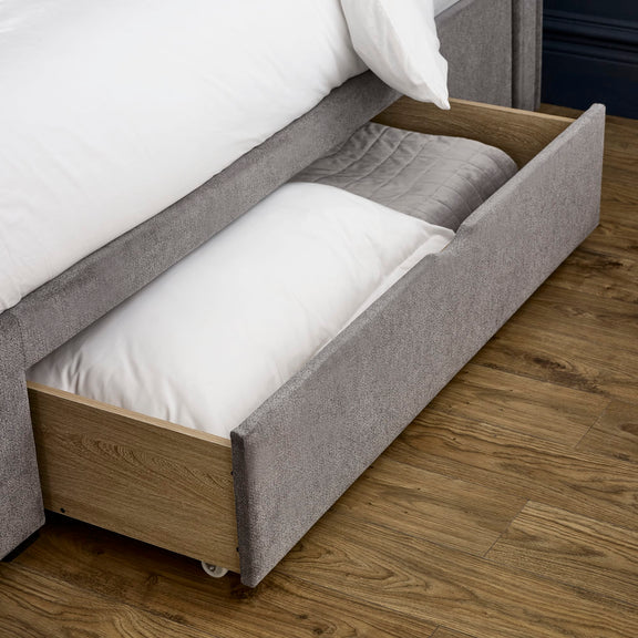 Gray upholstered bed with a wooden frame and white bedding on a wooden floor.