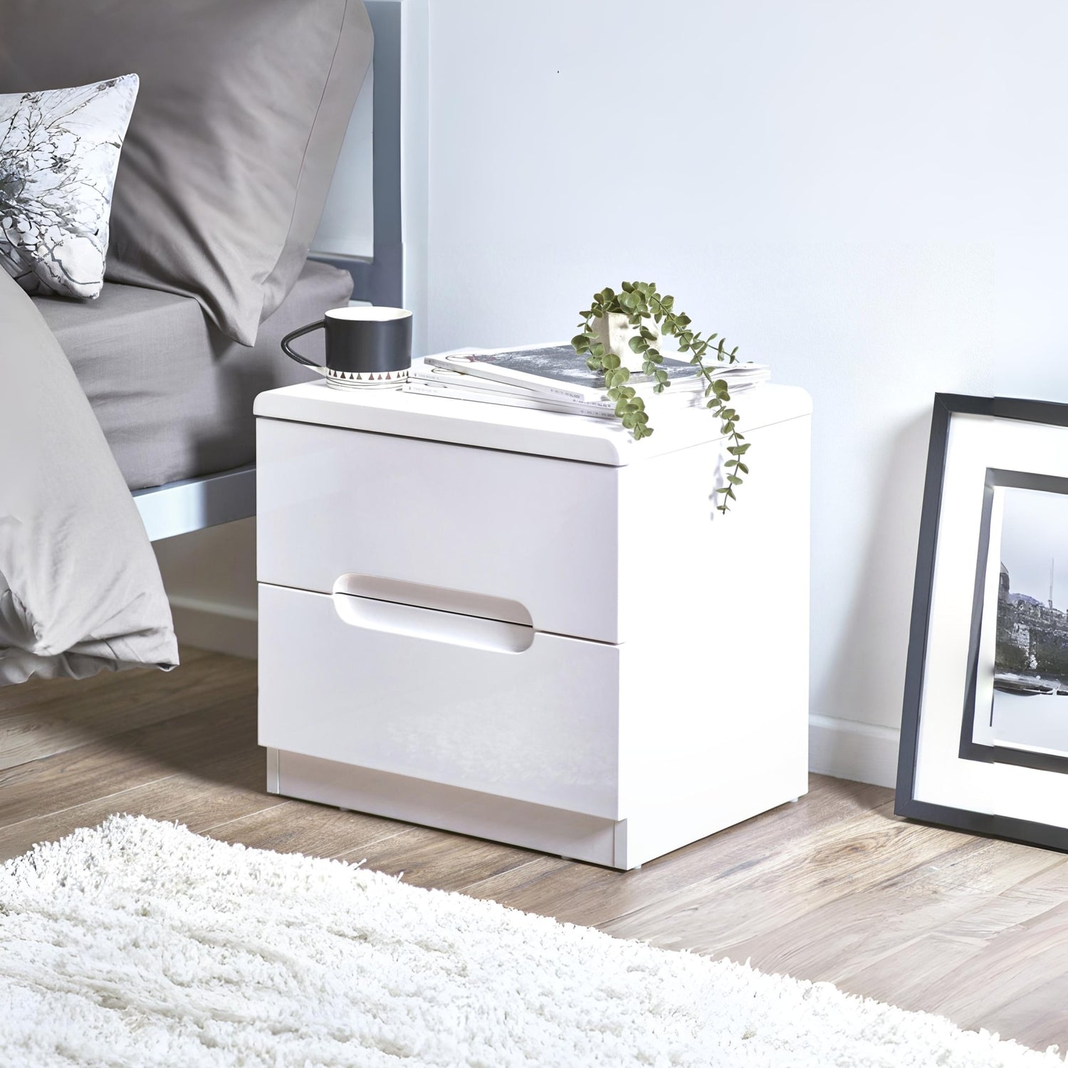 White nightstand with a lamp and plant in a bedroom setting