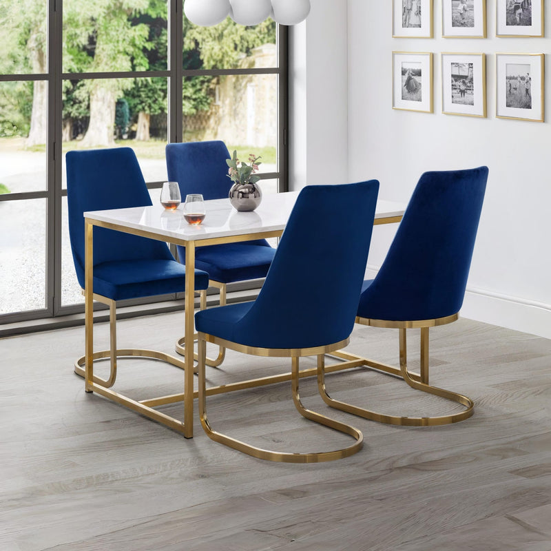 Dining room with blue chairs and a white table near large windows.