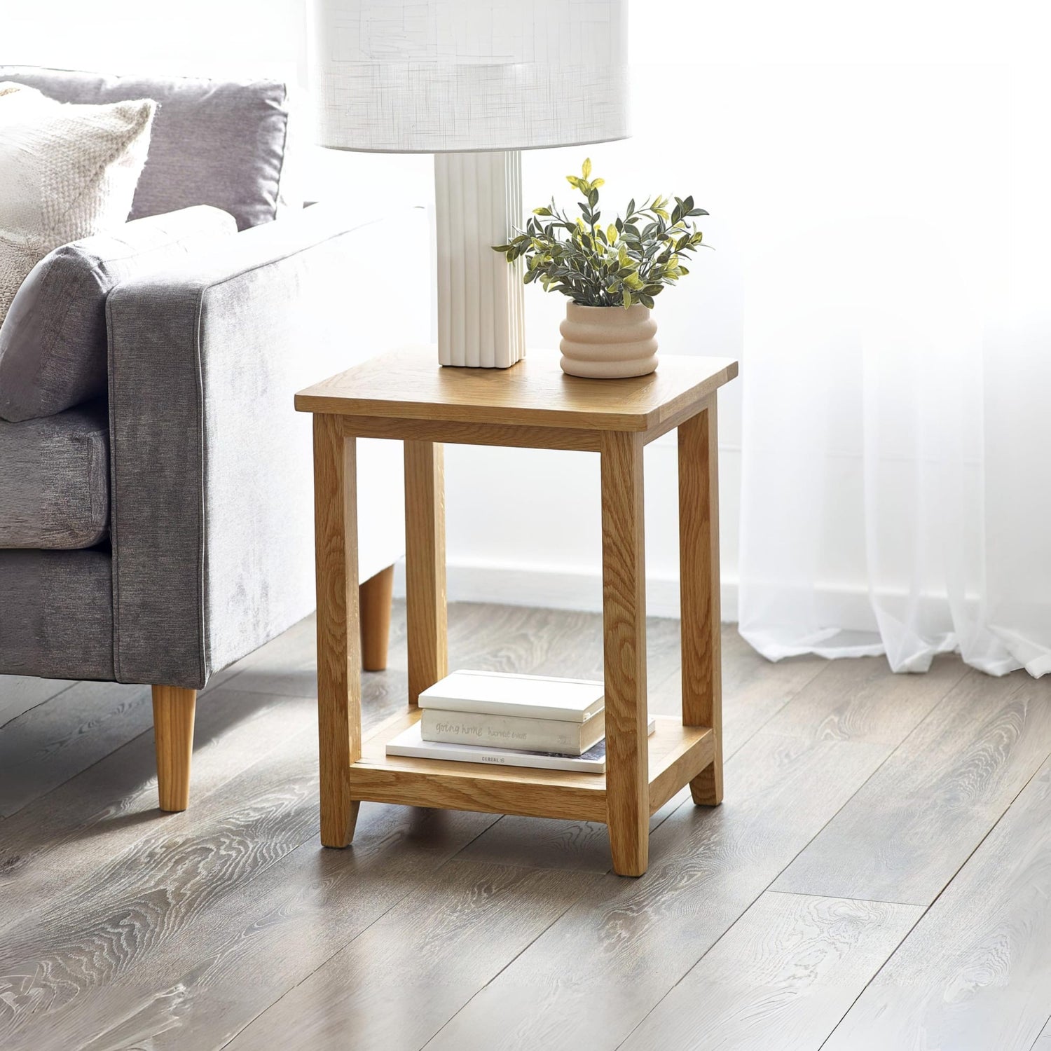 Wooden side table with lamp, books, and plant in a living room setting.