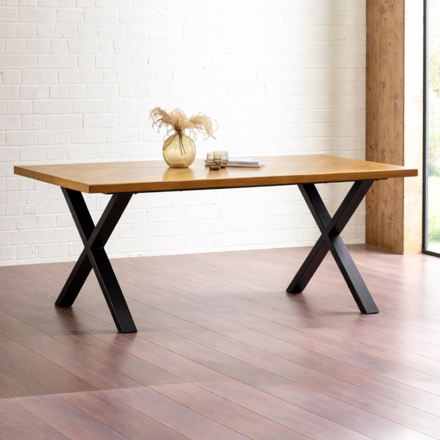 Wooden table with black metal legs in a room with wooden floor and white brick wall.