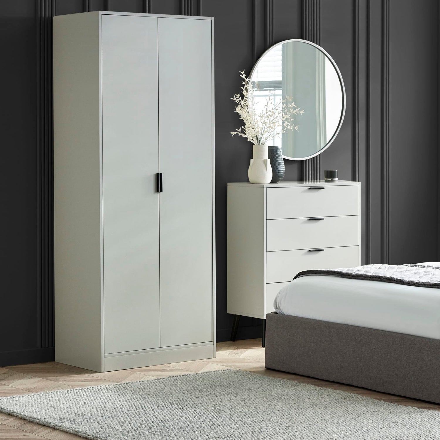 Gray wardrobe, dresser, and bed in a bedroom setting with a round mirror above the dresser.