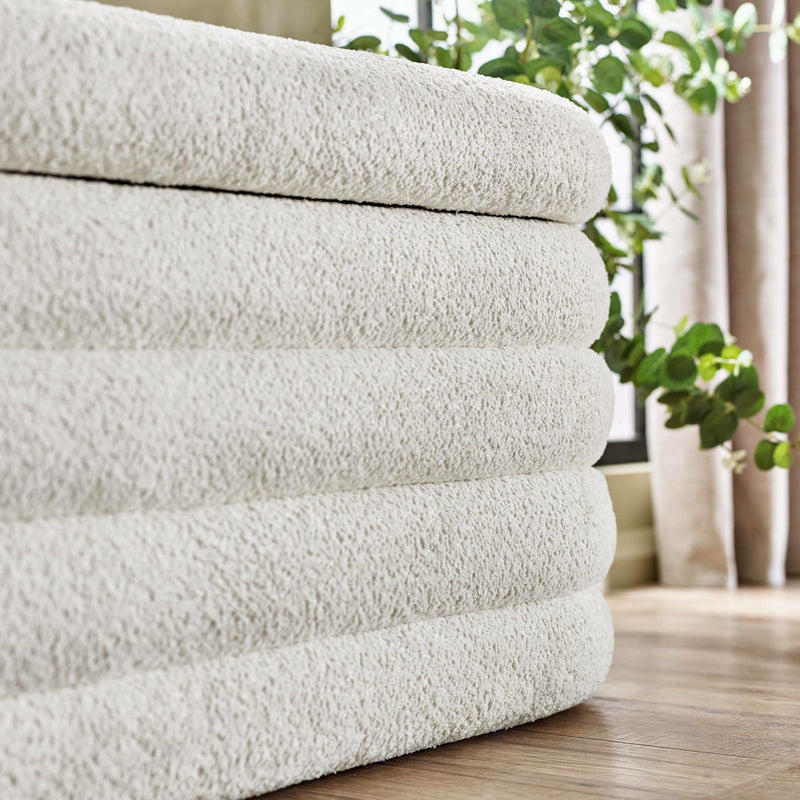 Stack of beige towels on a wooden floor with plants in the background