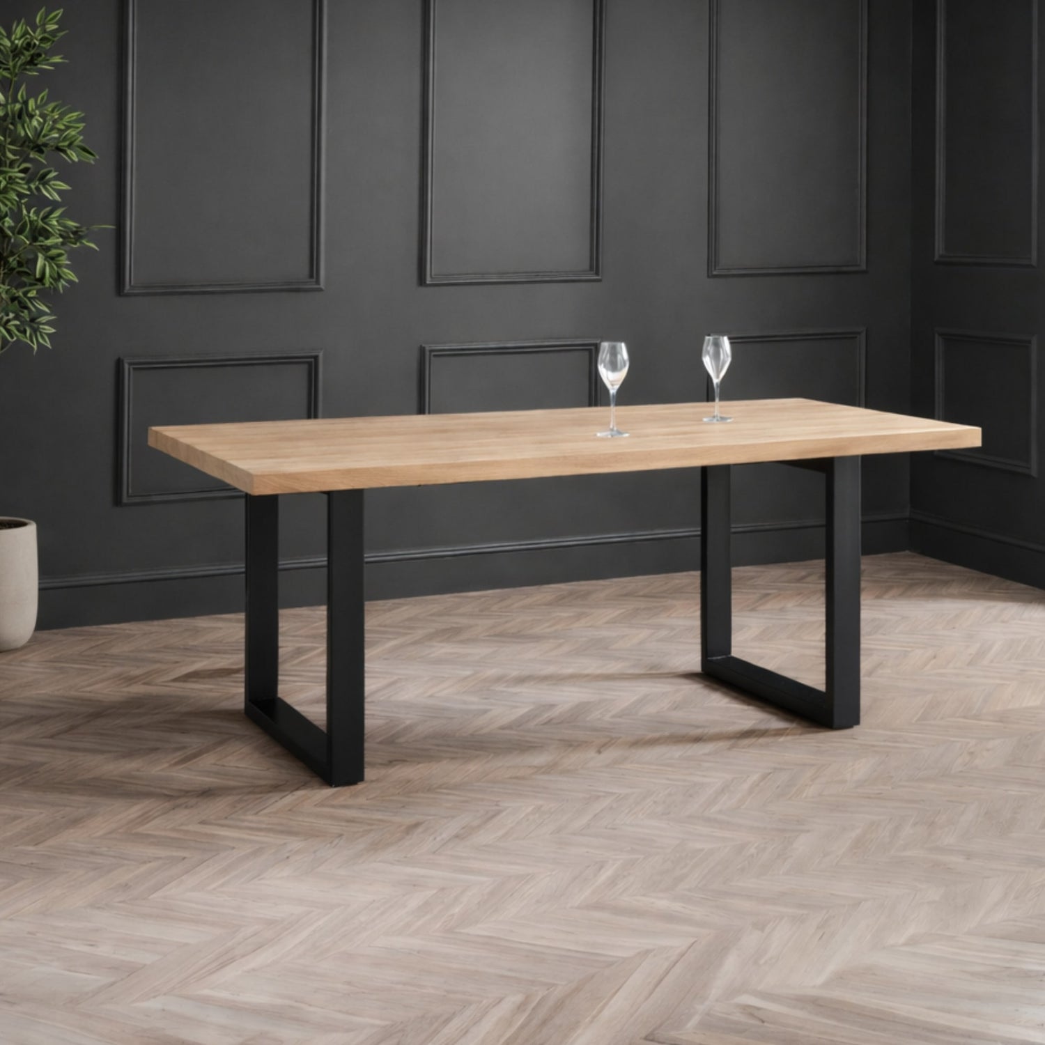 Wooden dining table with black legs in a room with dark paneled walls and wooden floor.
