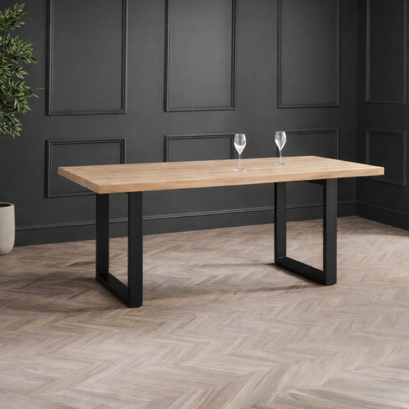 Wooden dining table with black legs in a room with dark paneled walls and wooden floor.