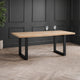 Wooden dining table with black legs in a room with dark paneled walls and wooden floor.