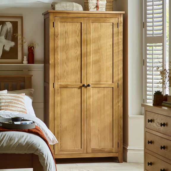 Wooden wardrobe in a bedroom setting with bed and dresser.