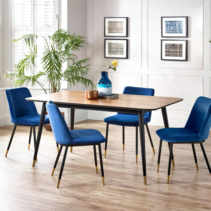 Dining room with a wooden table and blue chairs, featuring a plant and framed pictures on the wall.