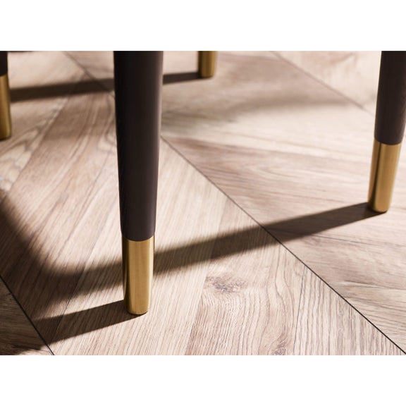 Close-up of a chair leg with black and gold finish on a wooden floor.