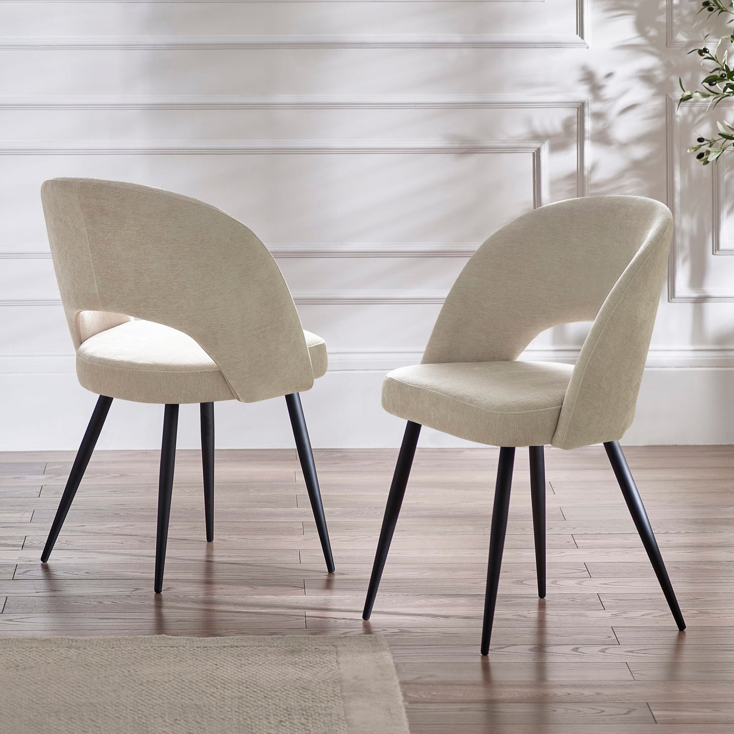 Two beige chairs with black legs on a wooden floor.