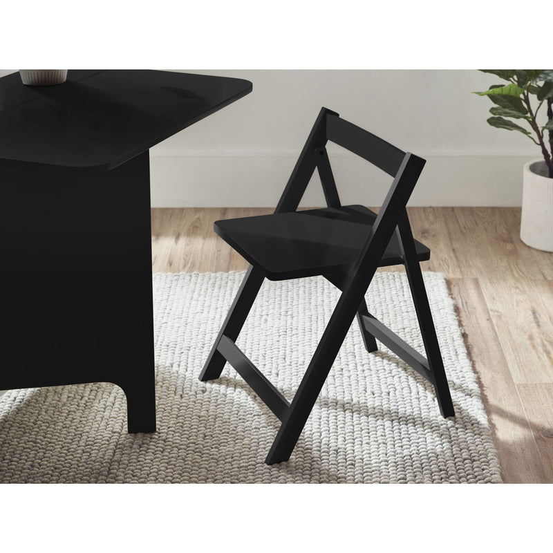 Black folding chair next to a black table on a wooden floor with a white wall in the background.