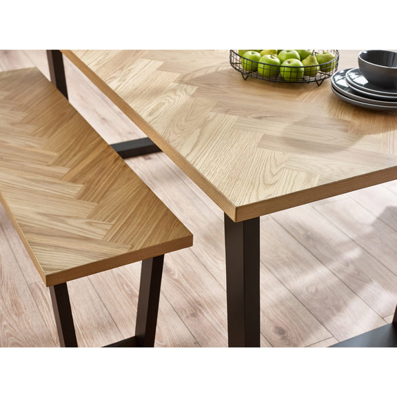 Wooden dining table with herringbone pattern and bench on a light wood floor.